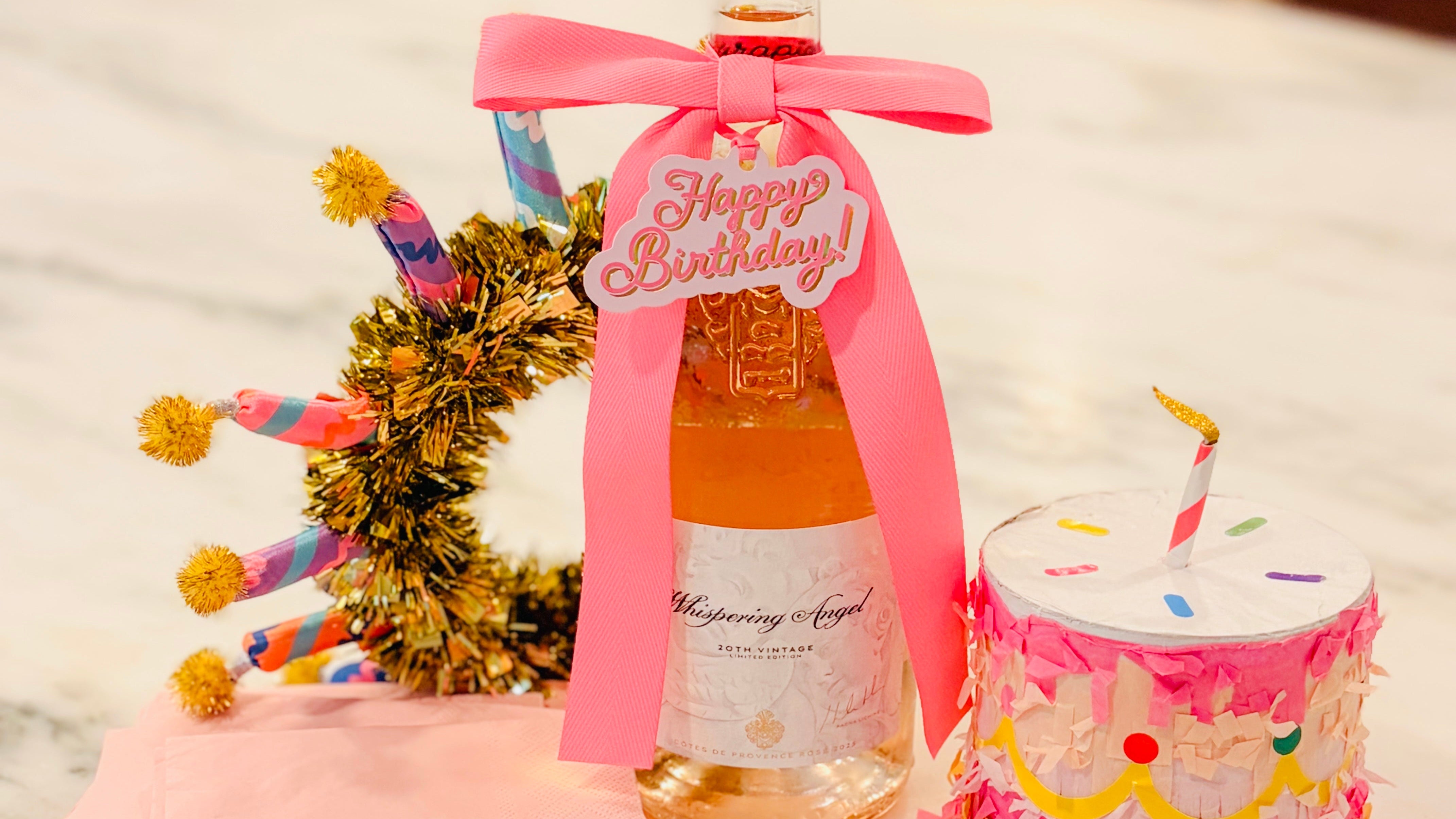 Bottle of wine with a pink ribbon and decorative elements on a marble surface.